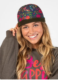 Woman wearing a colorful floral cap and a gray sweatshirt with 'Be Happy' text.