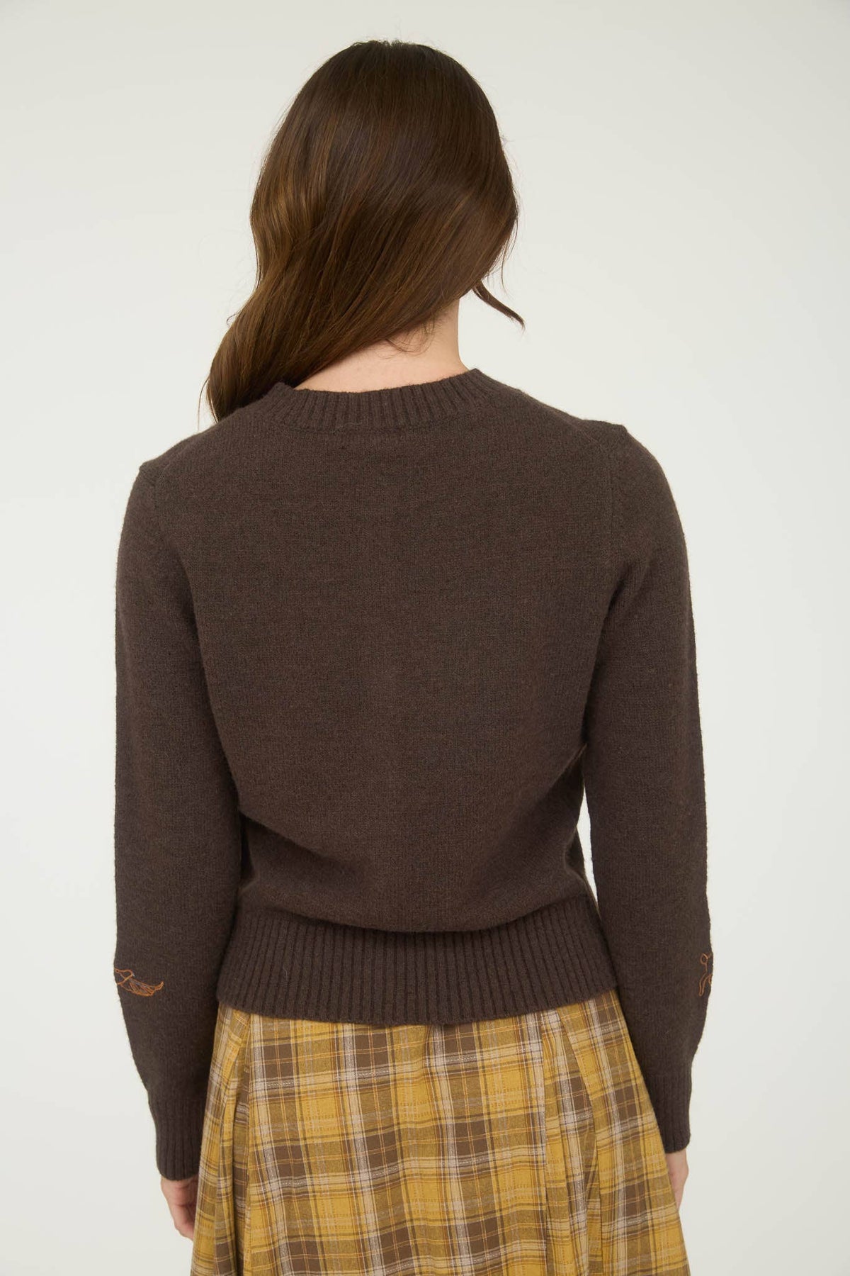 Person wearing a brown sweater and plaid skirt on a white background